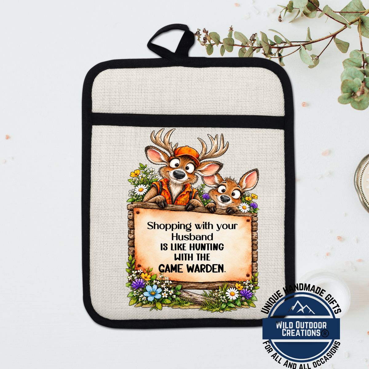 A beige oven mitt with a cartoon image of two deer and a sign that says "Shopping with your husband is like hunting with the came".
