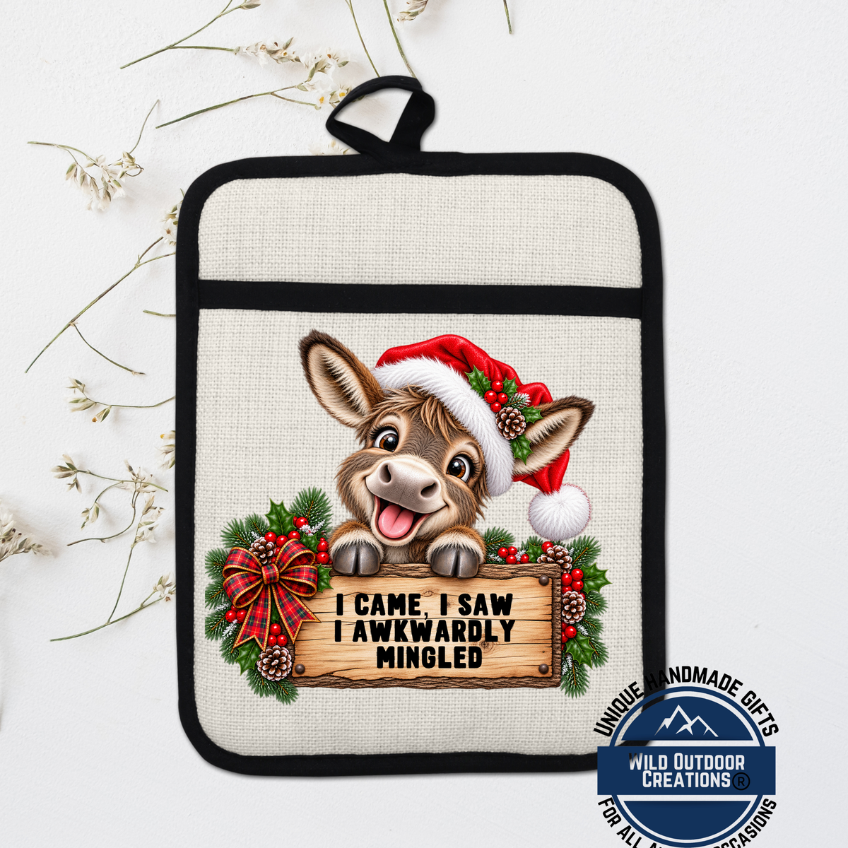 A pot holder with a cartoon donkey wearing a Santa hat and holding a sign that says "I came I saw I awkwardly mingled".