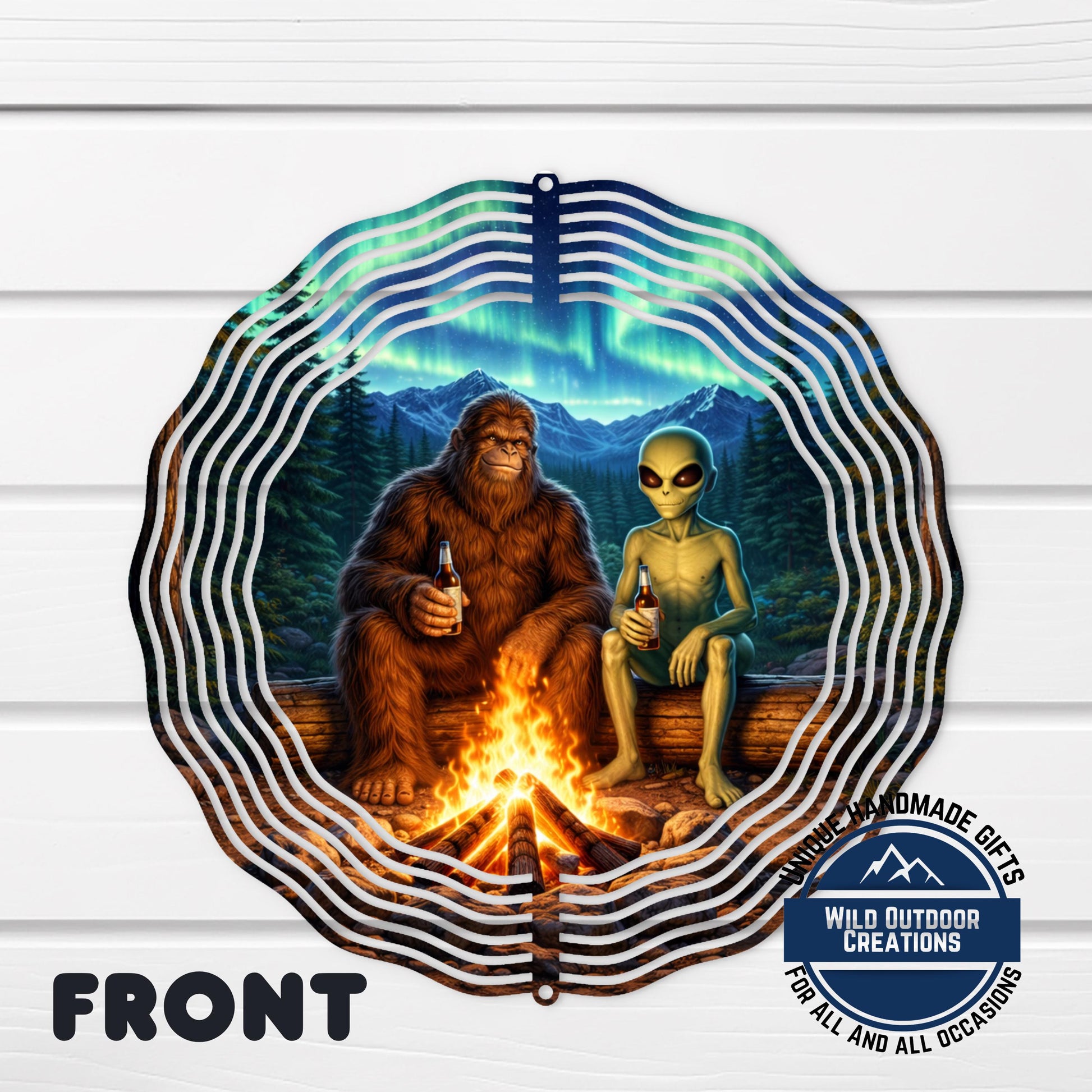 A large metal sculpture depicting a giant brown furry creature and a smaller alien sitting by a campfire in a forest setting, with a stunning night sky in the background.