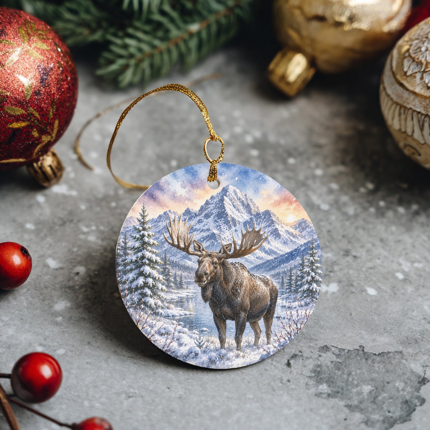 A circular ornament featuring a moose standing in a snowy forest, with mountains in the background.