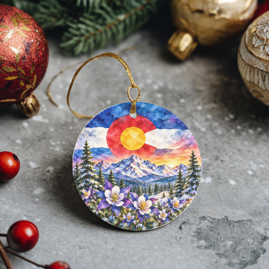 A round ornament featuring a colorful mountain landscape with a red sun, surrounded by flowers and pine trees.