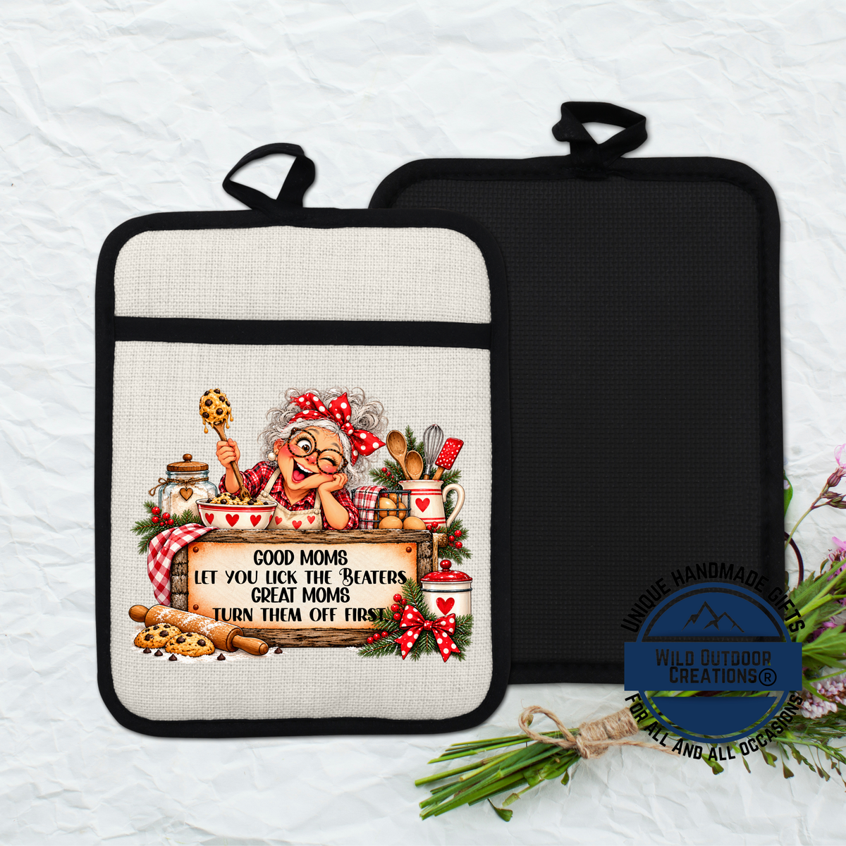 A beige oven mitt with a black handle, featuring an illustration of an elderly woman cooking and holding a sign that says "Good Moms let you lick the beaters, great mom, turn them off first".