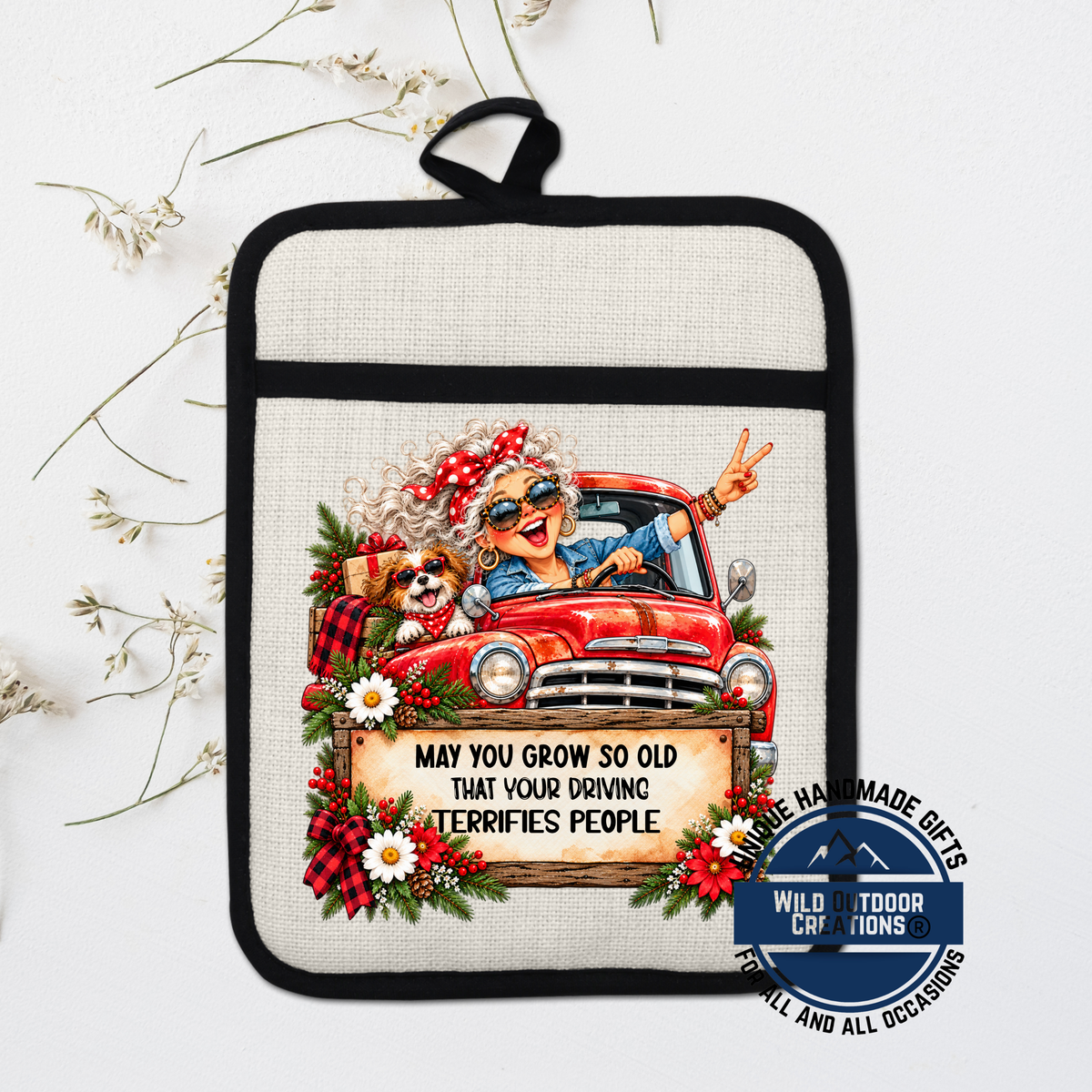 A hand-made pot holder with a cartoon image of an elderly woman driving a truck, surrounded by flowers and a sign that says "May you grow so old that your driving terrifies people".