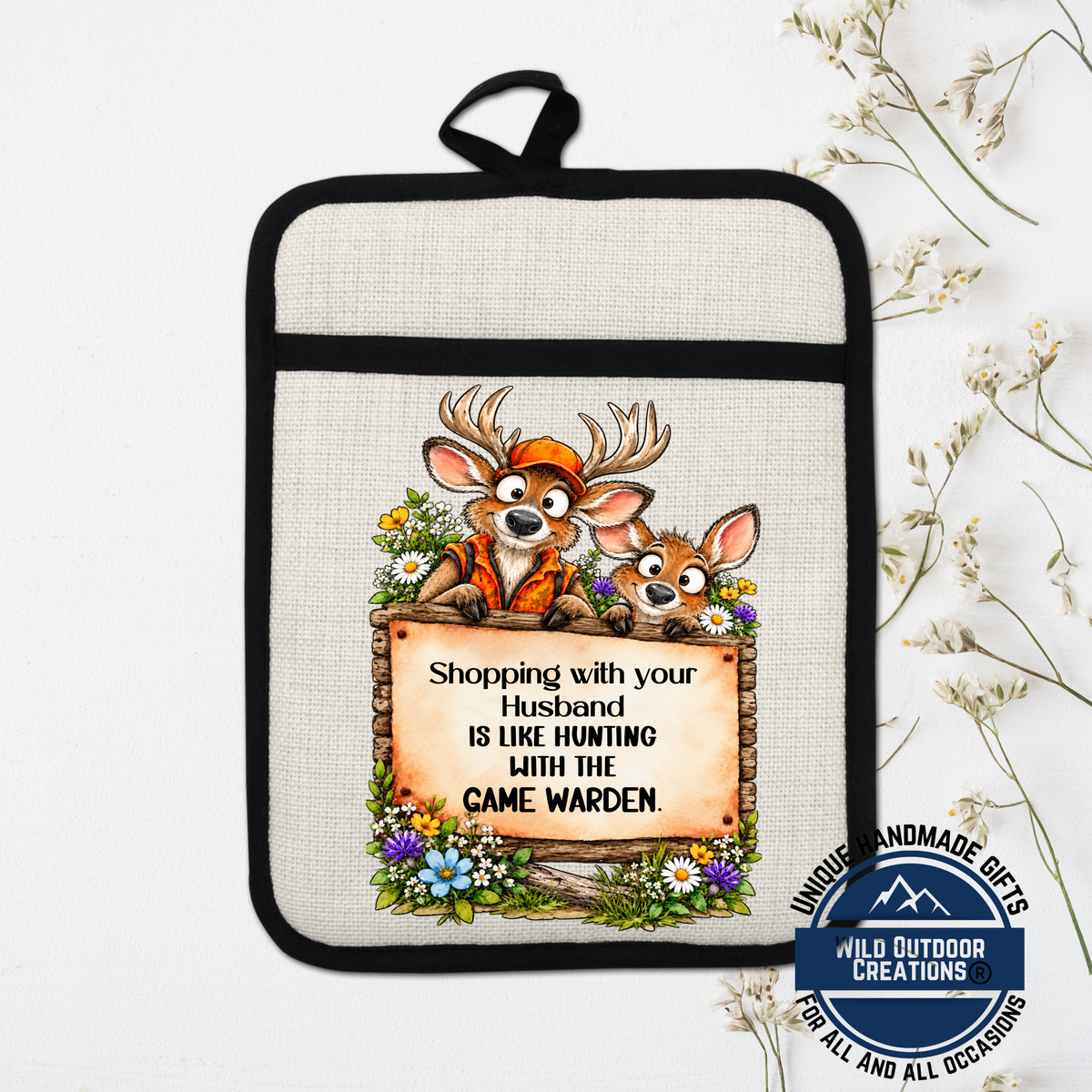 A beige pot holder with a cartoon image of two deer and a sign that says "Shopping with your husband is like hunting with the game warden".