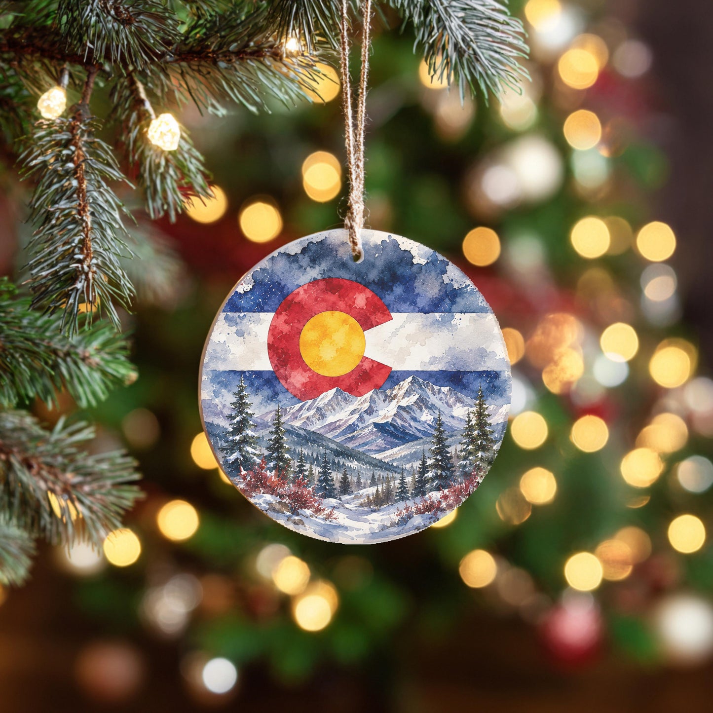 A circular ornament hanging on a Christmas tree, featuring a painting of a snowy mountain landscape with pine trees and a red and white flag in the center.