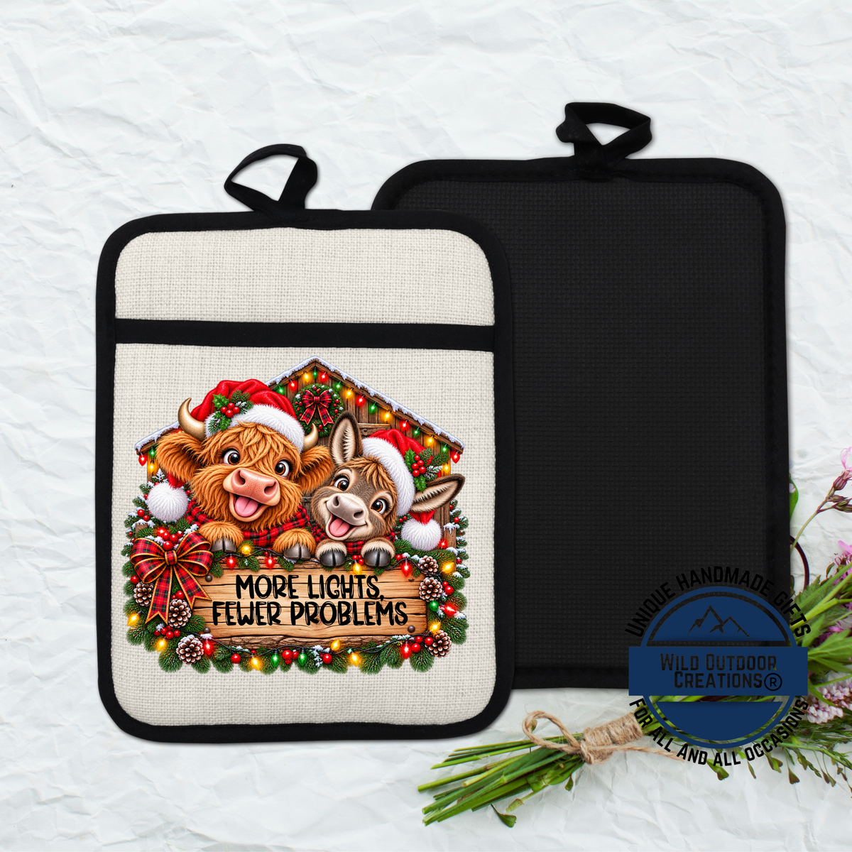 a kitchen pot holder with a Christmas-themed design, including two cartoon animals wearing Santa hats and surrounded by a wreath of lights and pine cones. The pot holder has a message that reads "MORE LIGHTS FEWER PROBLEMS" and is displayed on a white background.