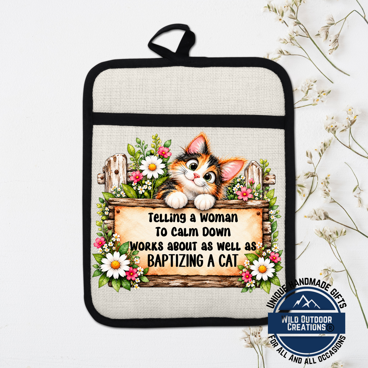 A hand-made pot holder with a cat illustration and a sign that says "Telling a woman to calm down works about as well as baptizing a cat".