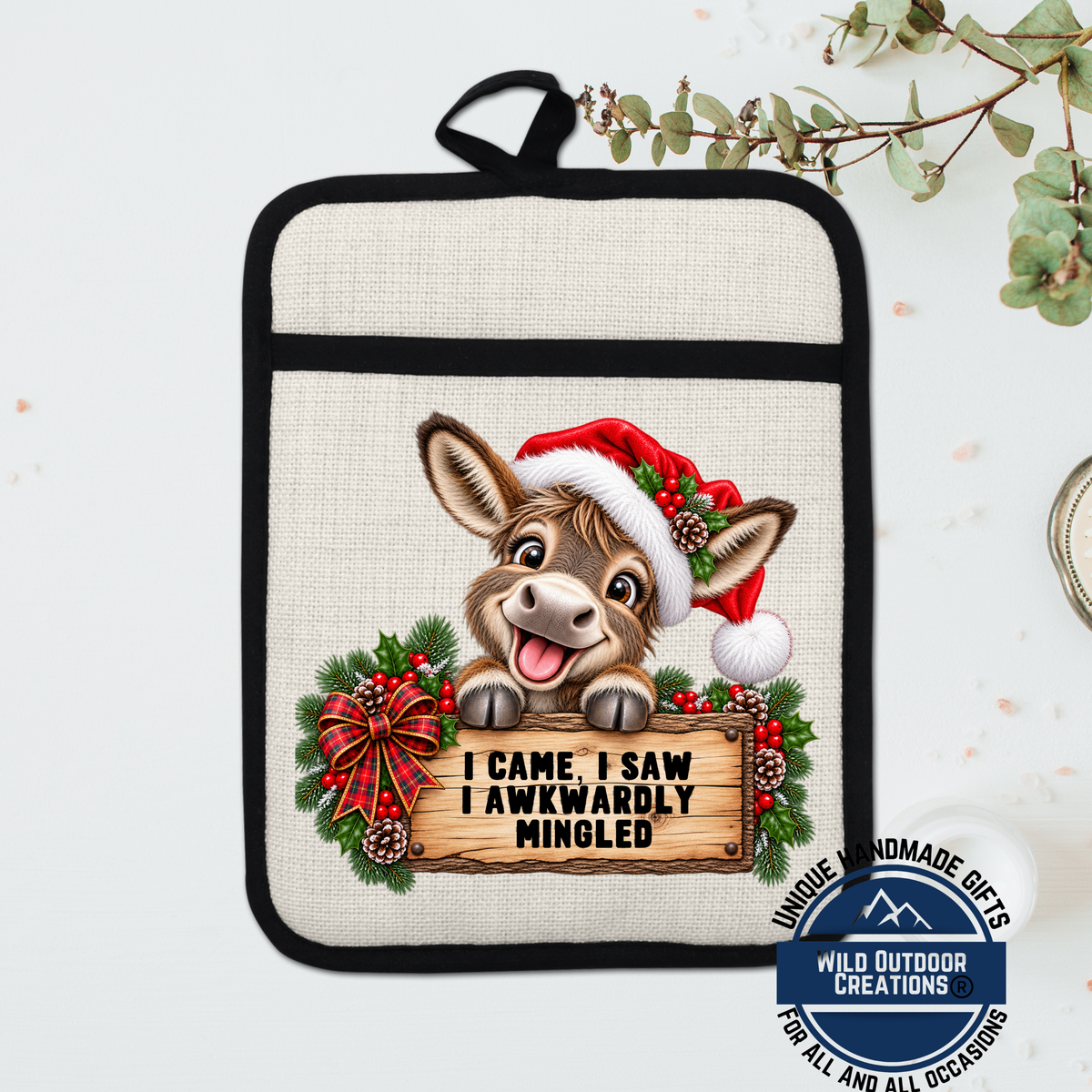 A beige pot holder with a cartoon donkey wearing a Santa hat and holding a sign that says "I Came, I Saw, I Awfully Minged".