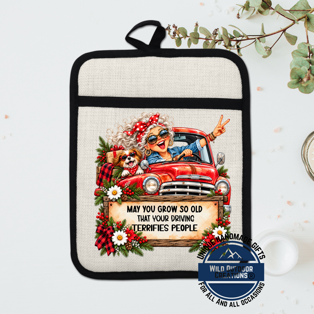 A hand-painted pot holder featuring an illustration of an elderly woman driving a red truck, with a sign that says "May you grow so old that your driving terrifies people".