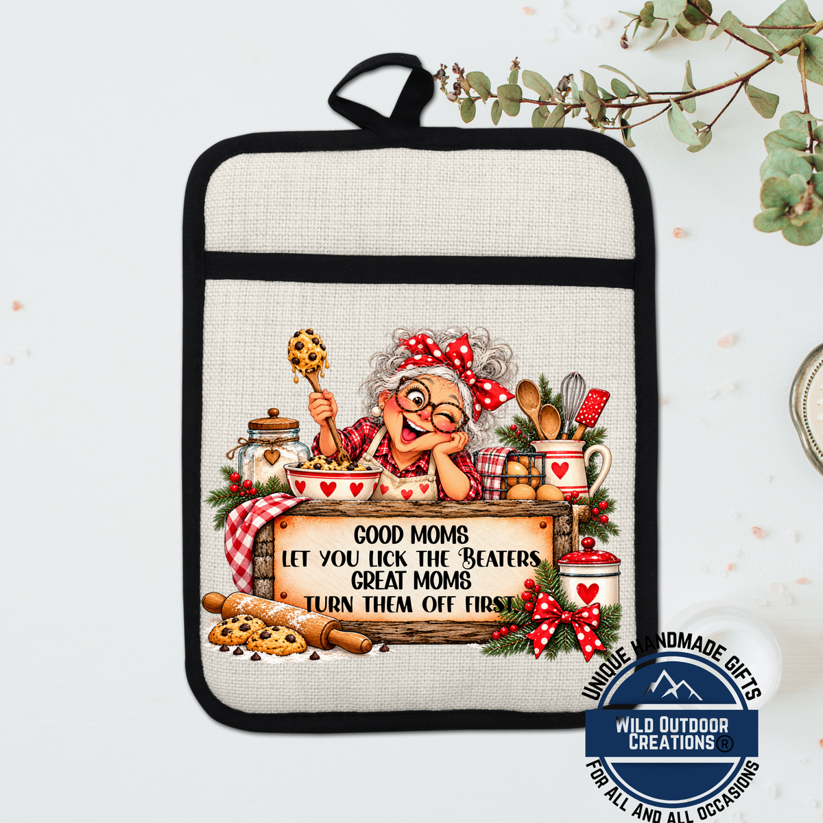 A hand-painted pot holder featuring an illustration of an elderly woman cooking, with a sign that says "Good Moms let you lick the beaters, great mothers turn them off first".