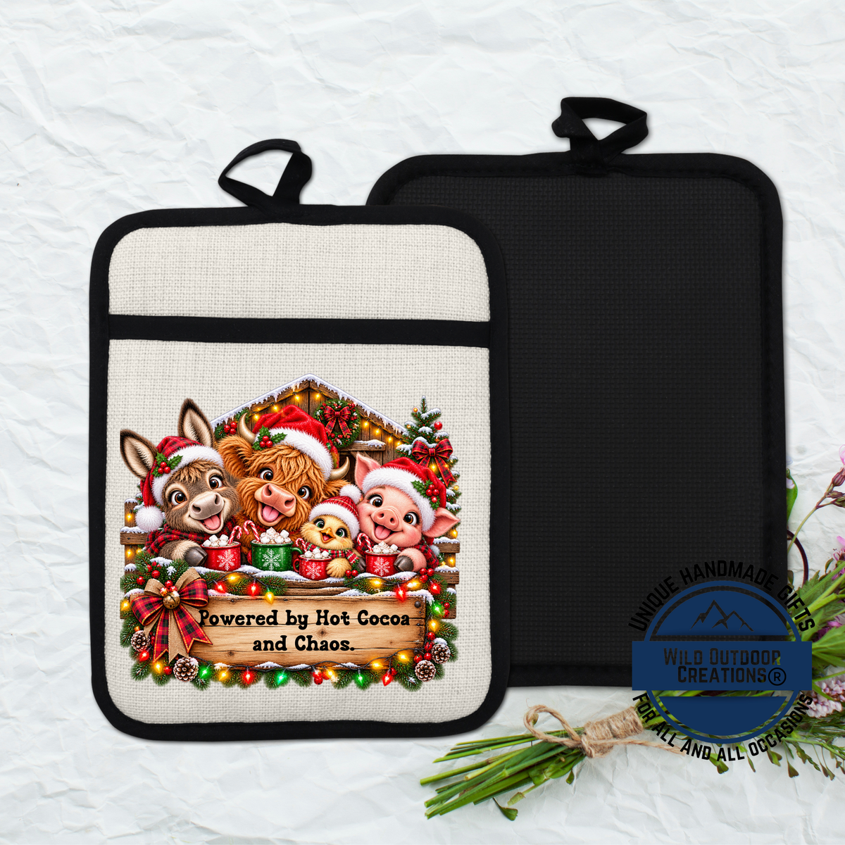 A kitchen pot holder with a festive Christmas-themed design featuring animals, such as a pig, donkey, and chicken, along with a sign that says "Powered by Hot Cocoa and Chaos".