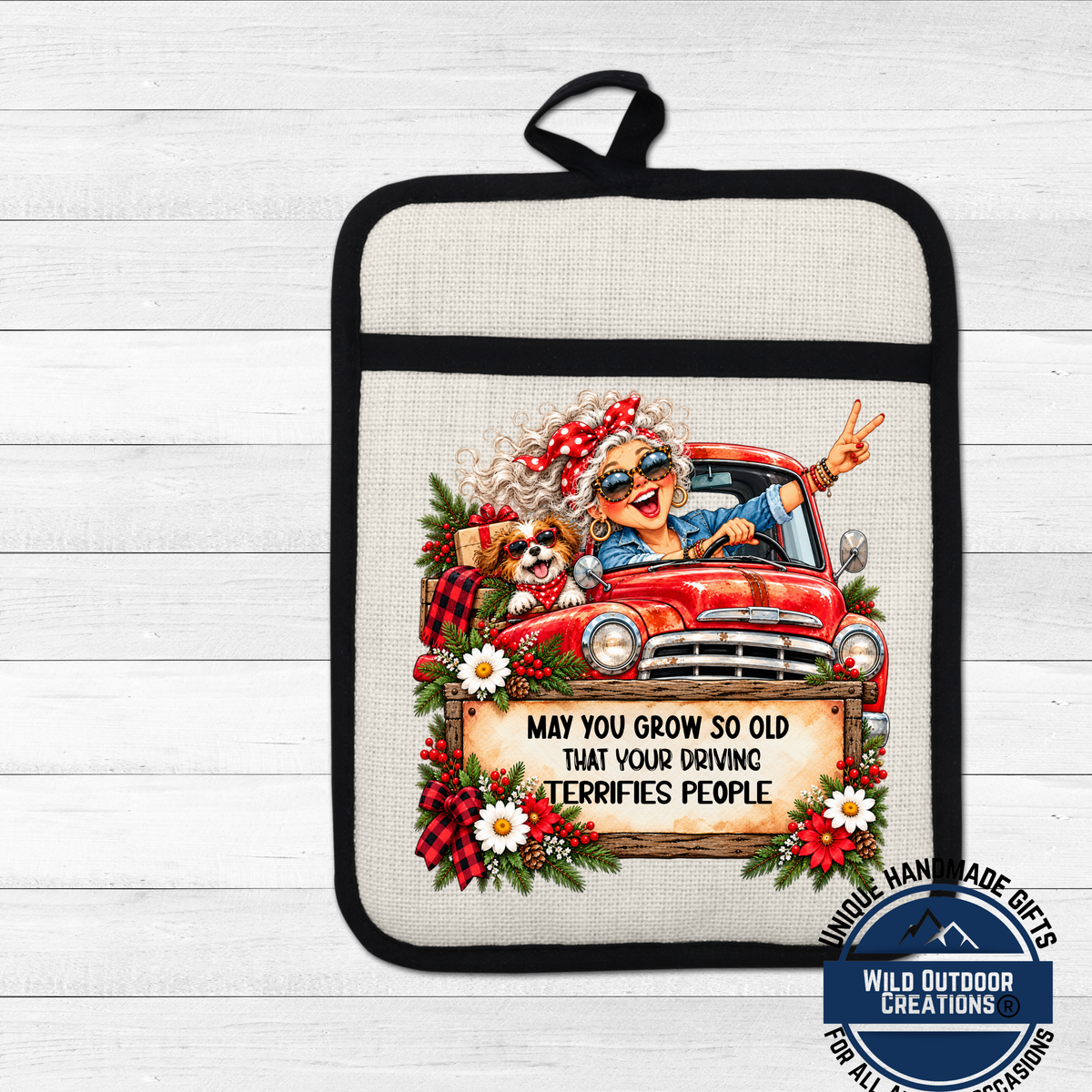 A hand-made pot holder featuring an illustration of an elderly woman driving a red truck, with a dog in the back seat. The pot holder has a humorous message that reads "May you grow so old that your driving terrifies people".