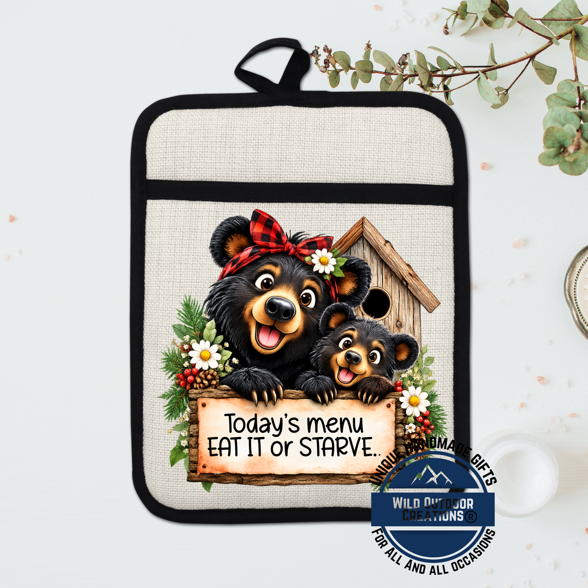 A kitchen pot holder with a cartoon image of two bears, one larger and one smaller, peeking out from behind a sign that says "Today's menu eat it or Starve."