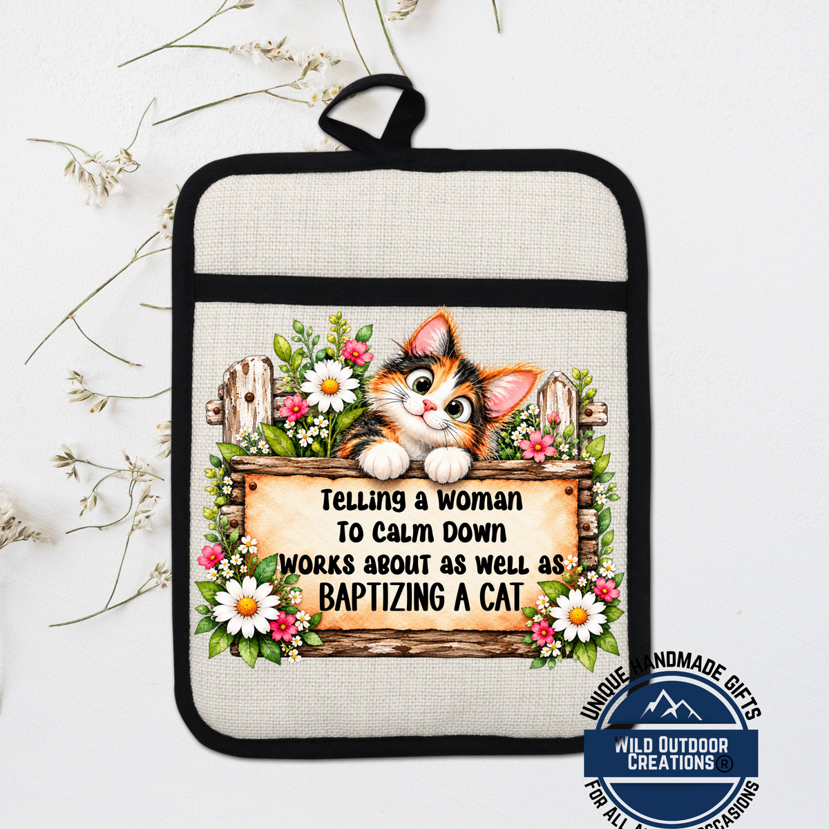 A hand-made pot holder with a cat illustration and text that says "Telling a woman to calm down works about as well as baptizing a cat".