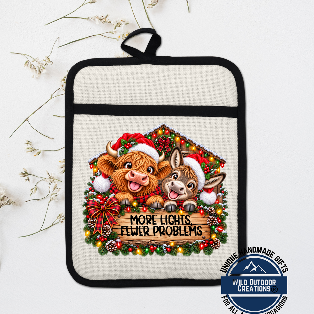 A beige pot holder with a Christmas-themed design featuring two cartoon cows wearing Santa hats and surrounded by a wreath of lights and pine cones. The text on the pot holder reads "MORE LIGHTS FEWER PROBLEMS".