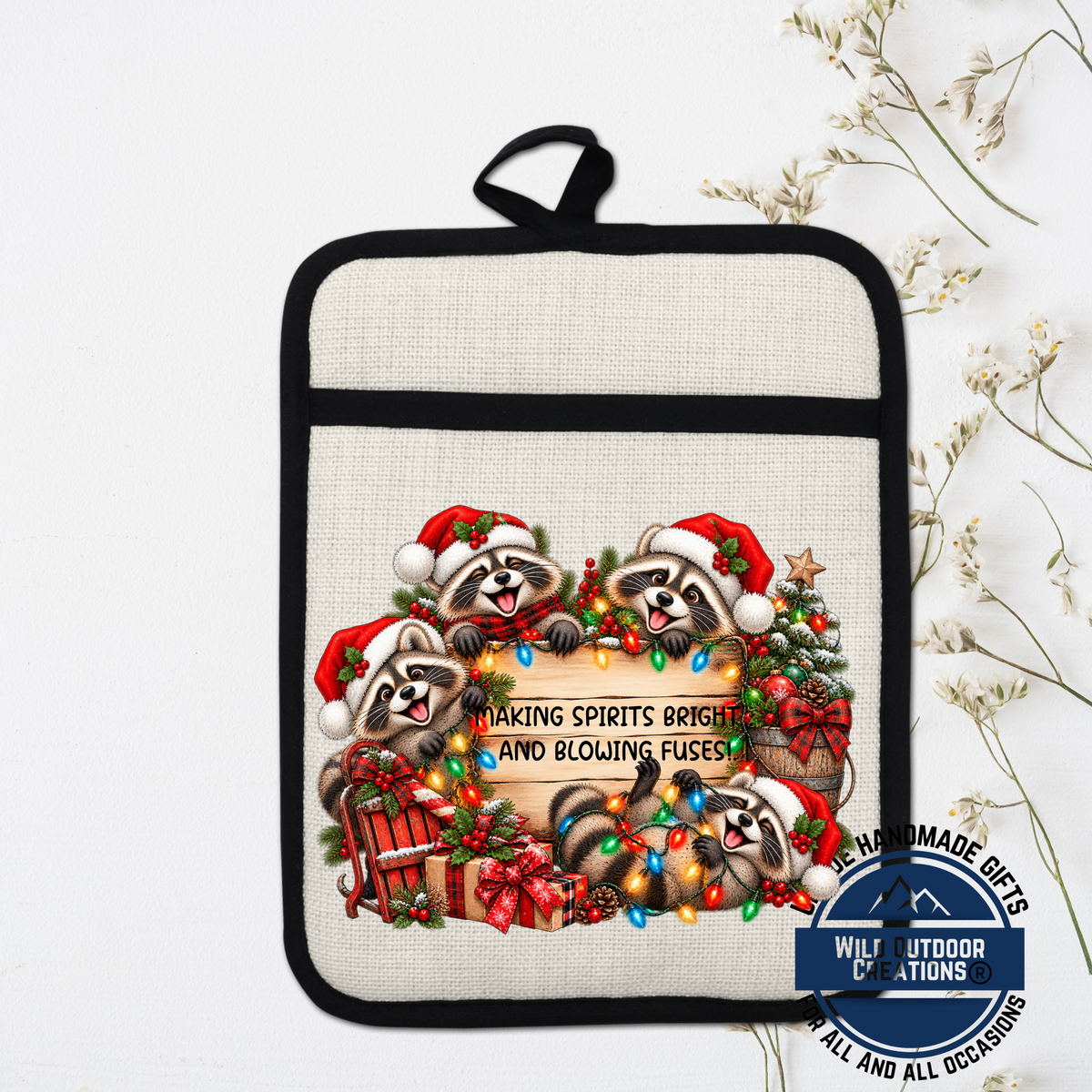 A beige pot holder with a black handle, featuring a festive Christmas-themed design with raccoons wearing Santa hats and surrounded by holiday decorations such as Christmas lights, ornaments, and a wreath.