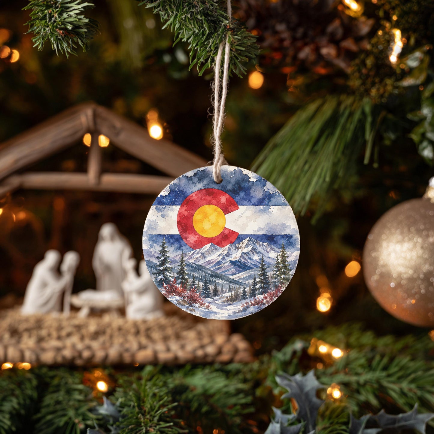 A round ornament with a Colorado flag design hangs from a Christmas tree, surrounded by other ornaments and lights.