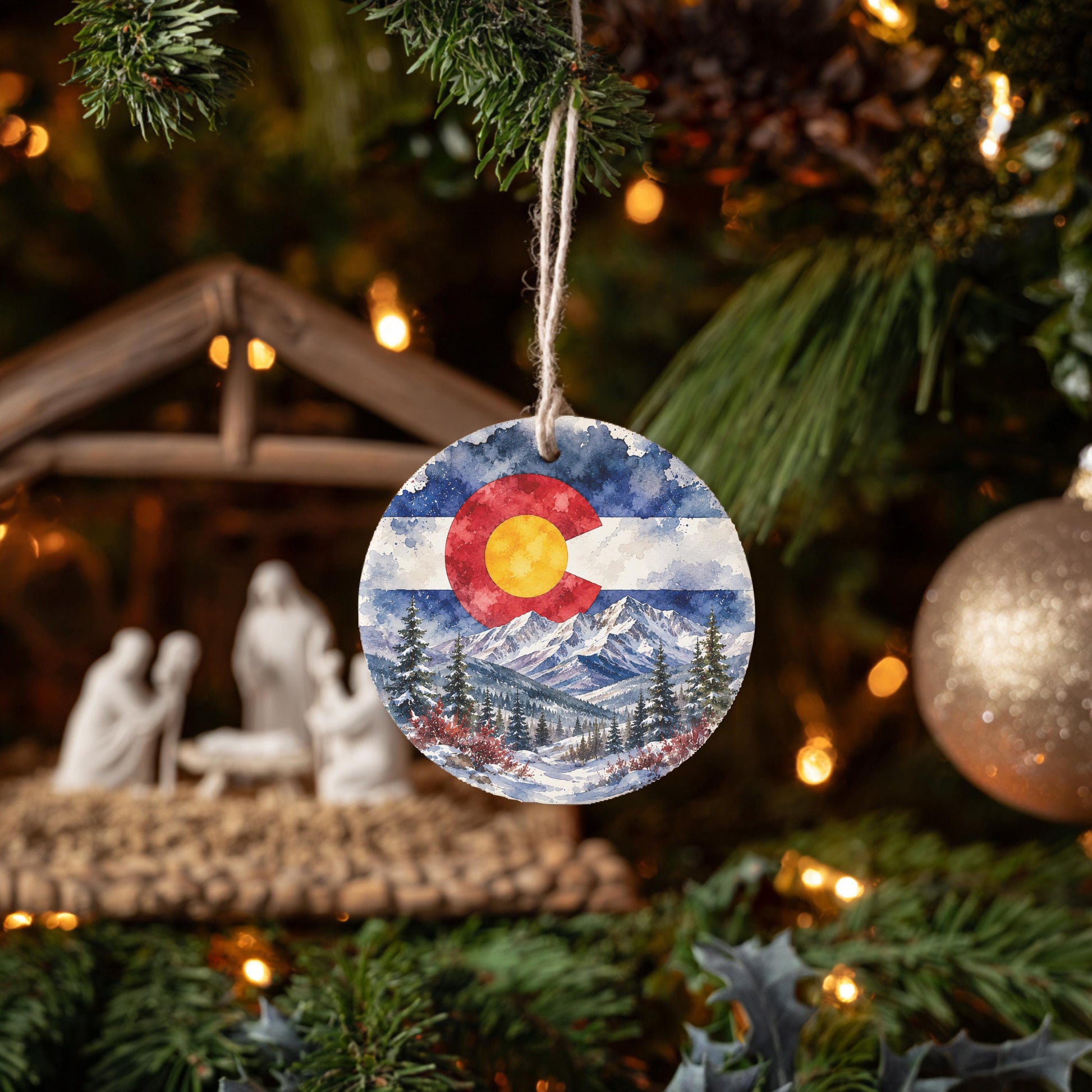 A round ornament with a Colorado flag design hangs from a Christmas tree, surrounded by other ornaments and lights.