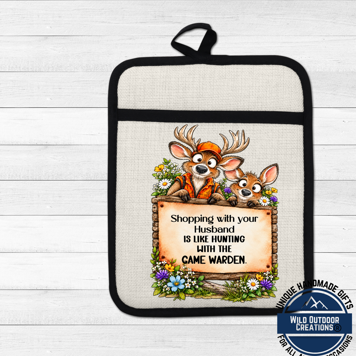 A beige oven mitt with a cartoon image of two deer and a sign that says "Shopping with your husband is like hunting with the game warden".