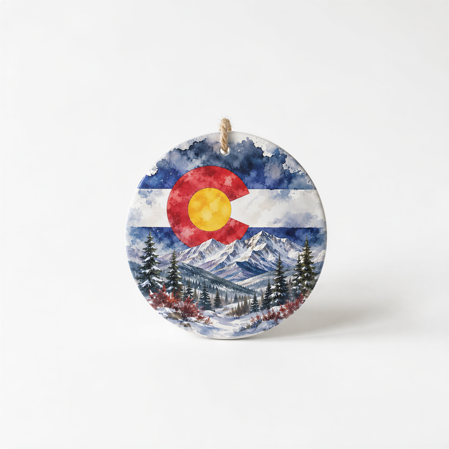 A circular ornament featuring a watercolor painting of a snowy mountain landscape with pine trees and a large red and yellow sun in the sky.