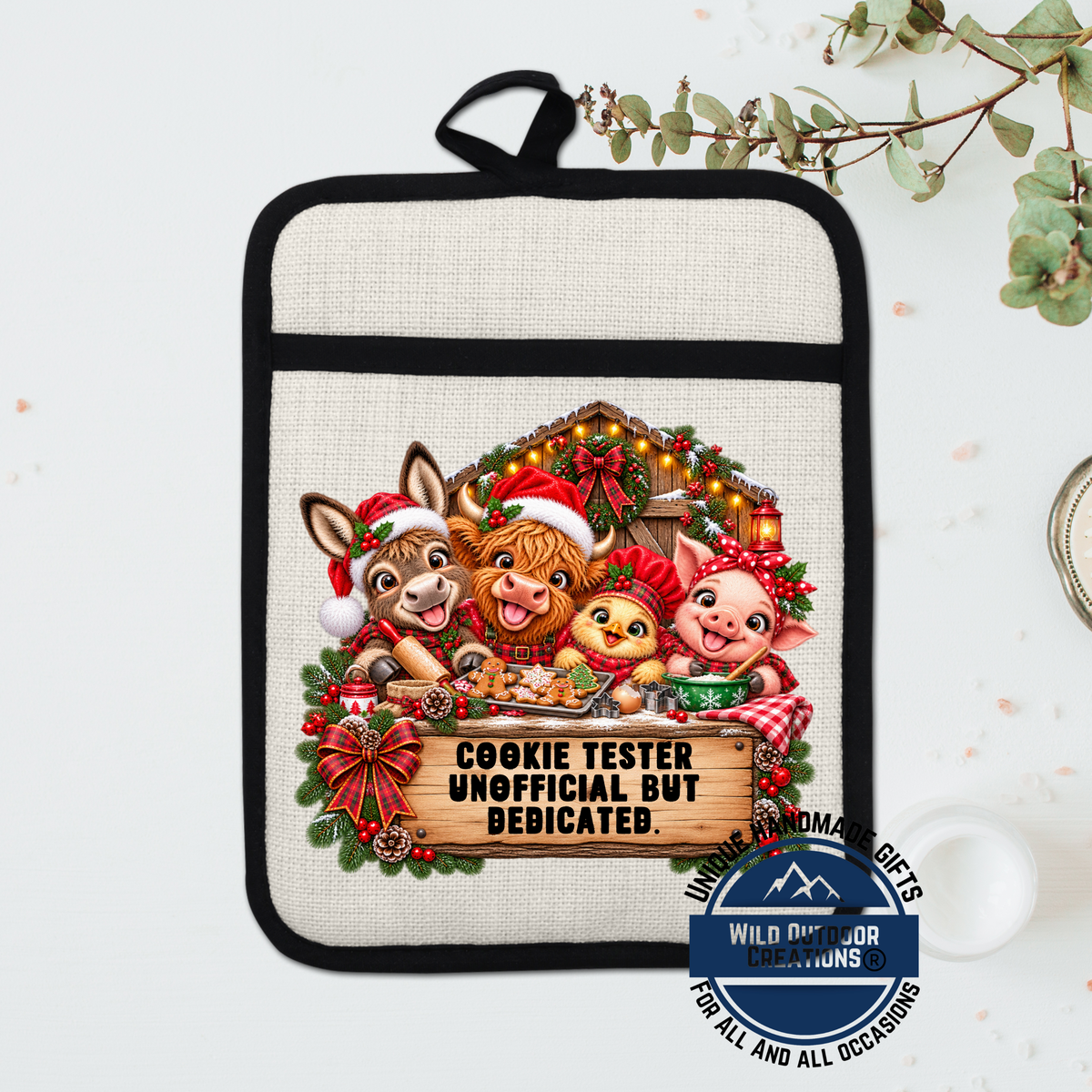 A beige oven mitt with a cartoon illustration of a cow, pig, and chicken, along with a sign that says "COOKIE TESTER UNOFFICIAL BUT BEDICATED."